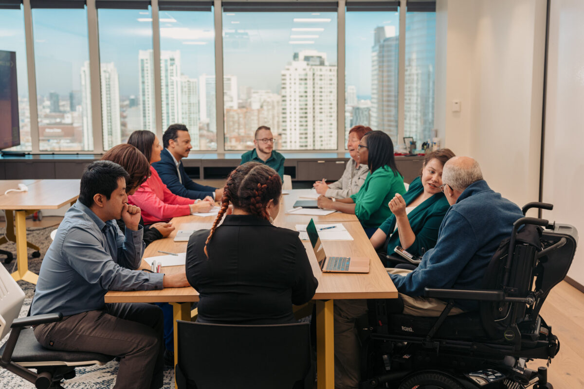 A diverse group of professionals are gathered around a conference room table. Image courtesy of Disability:IN.